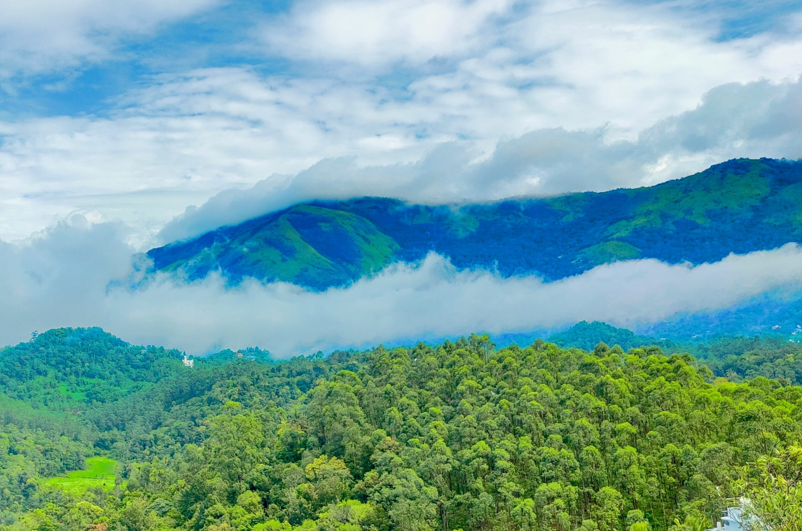 A landscape with mountains, clouds and green trees.